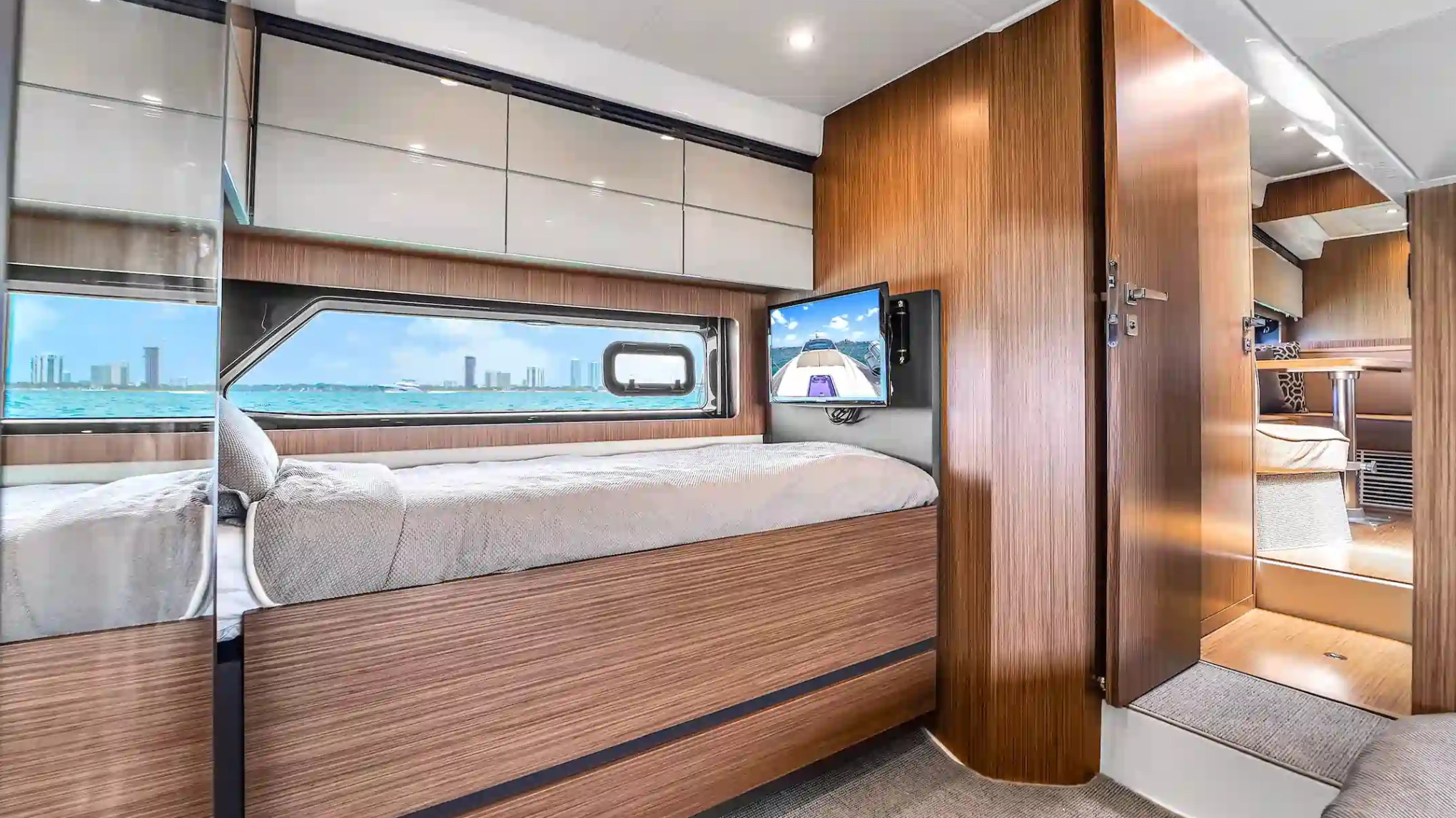Modern yacht bedroom with wood paneling, bed, TV, and window view of cityscape.