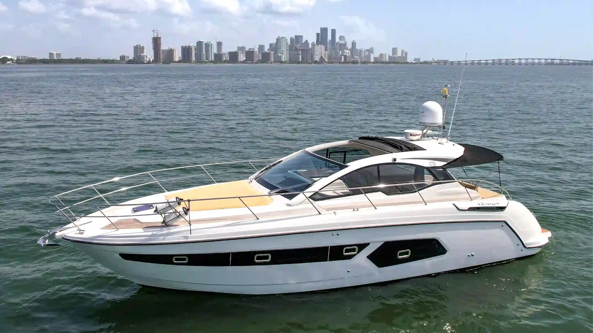 Luxury yacht on water with city skyline in background under clear sky.