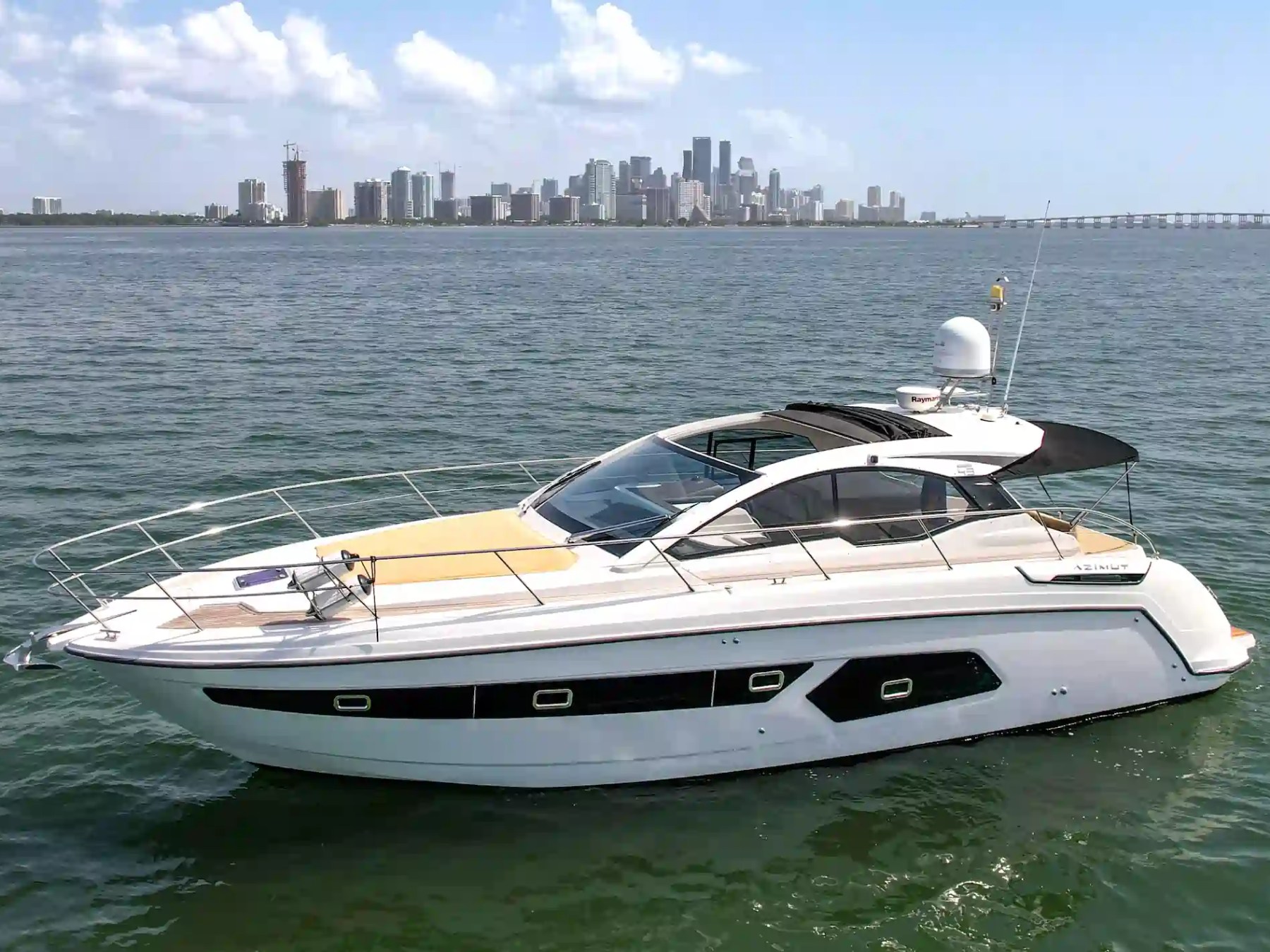 Luxury yacht on water with city skyline in background under clear sky.