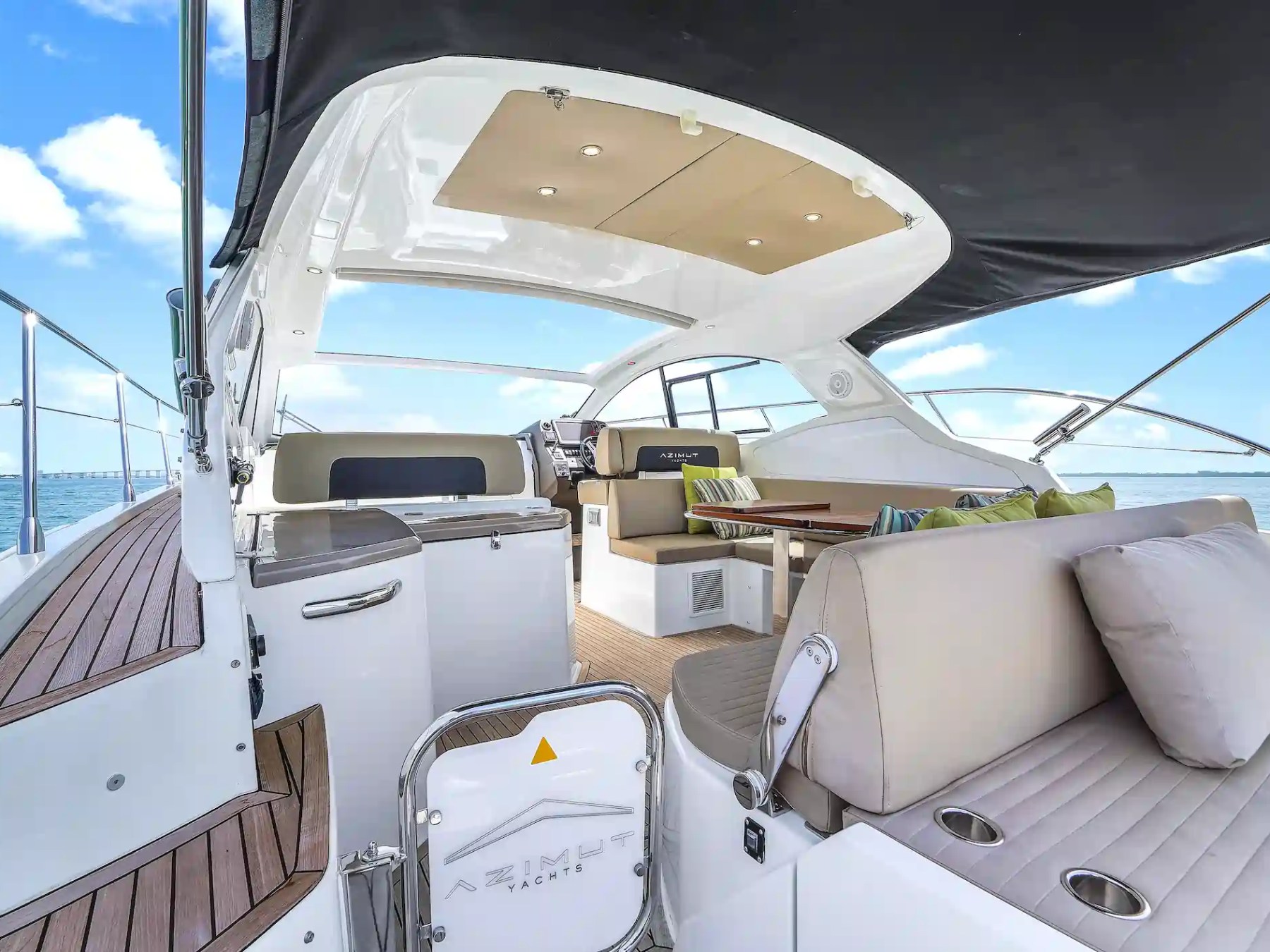 Luxury yacht deck with seating area, cushions, and table under a canopy on a sunny day.