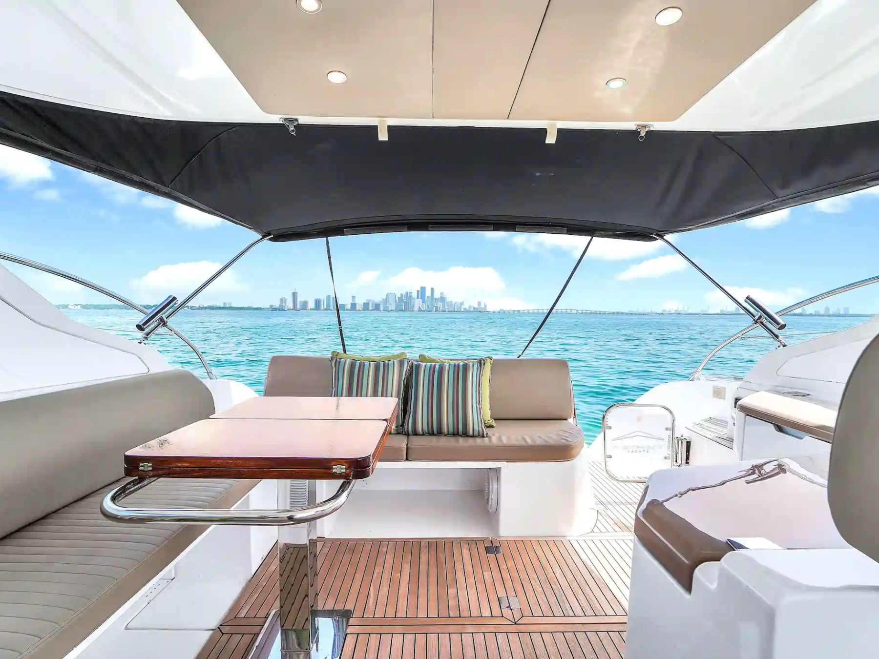 View from yacht deck with seating, table, and city skyline in background.