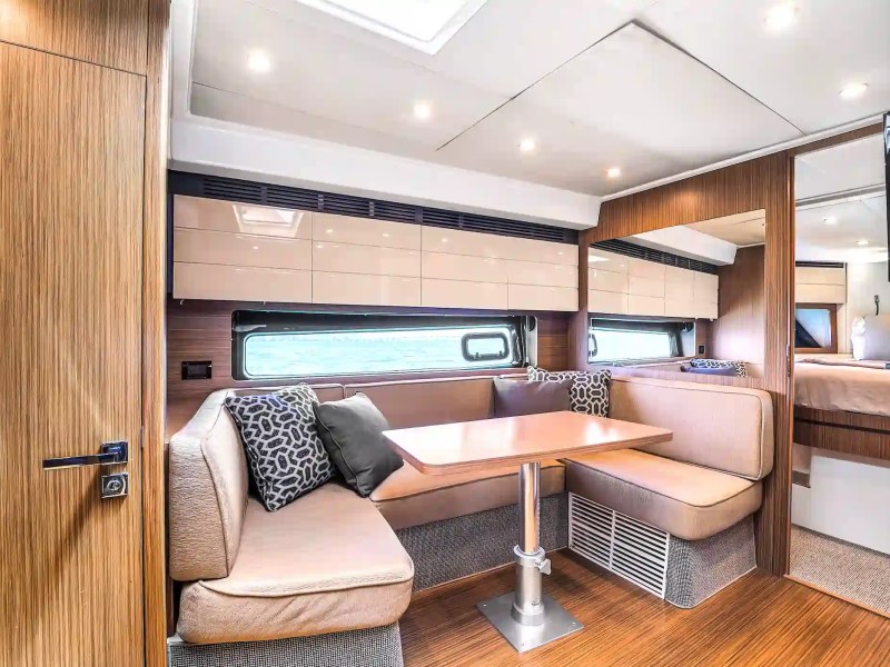 Modern RV interior with a dining area, cushions, and overhead cabinets.