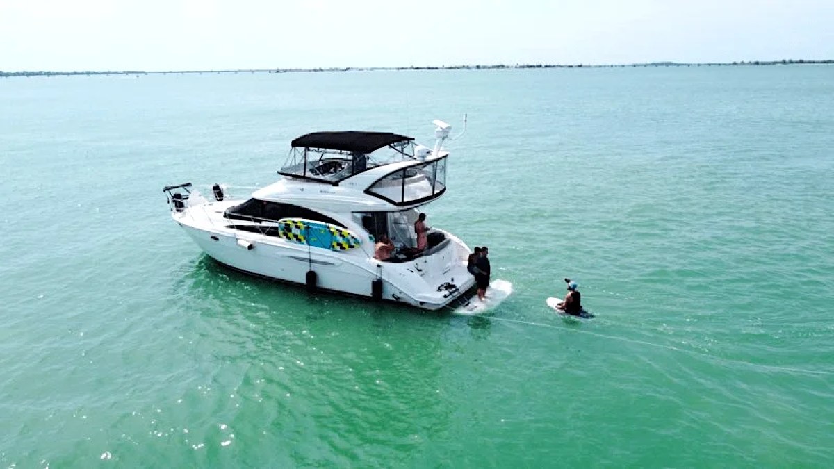 This 44 foot Meridian Boat Rental is anchored in clear turquoise Southwest Florida waters near Cape Coral with guests enjoying the swim platform and relaxing beside the vessel.