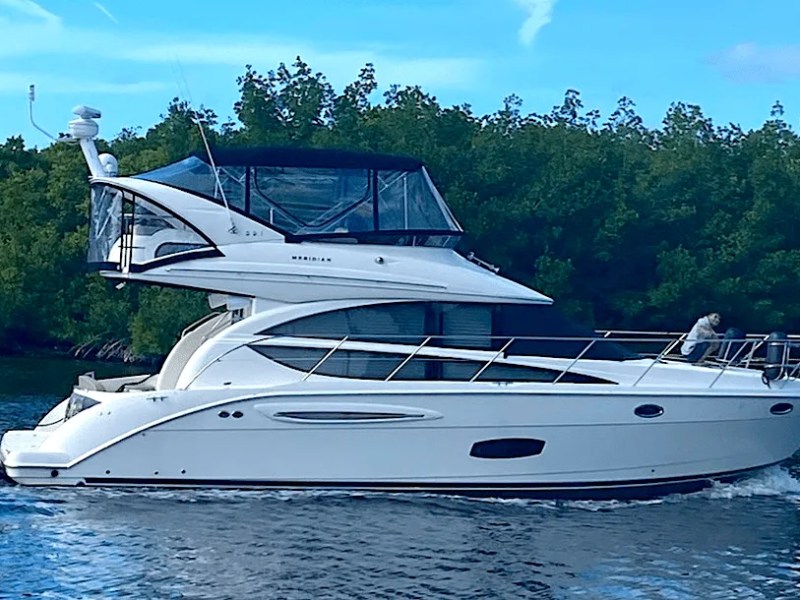 This 44 foot Meridian Boat Rental cruises through Cape Coral waterways with a sleek flybridge profile, enclosed upper deck, and mangrove-lined Southwest Florida shoreline in view.
