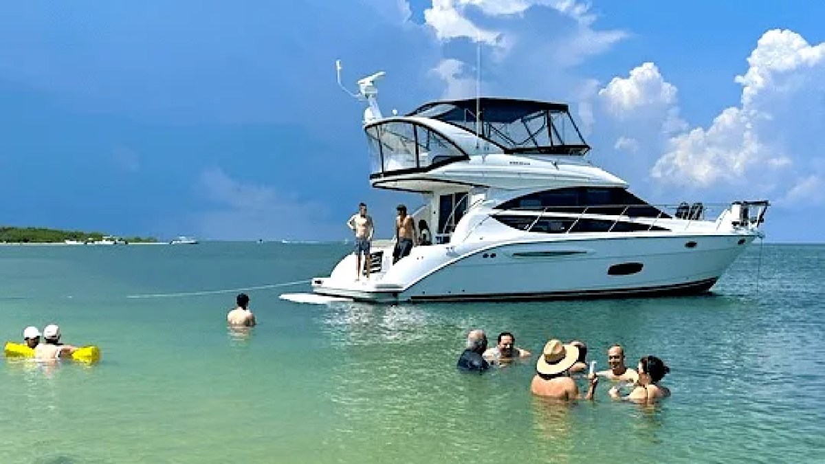 This 44 foot Meridian Boat Rental is anchored in shallow turquoise waters near Cape Coral with guests swimming beside the vessel and relaxing under sunny Southwest Florida skies.