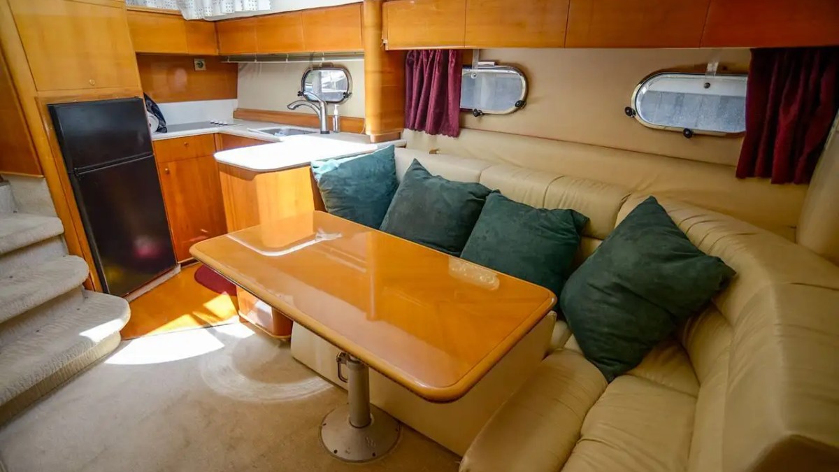 This 50 foot Viking Yacht Charter features a lower dining lounge with wraparound leather seating, wood cabinetry, galley access, and portlight windows while cruising near Cape Coral, Florida.