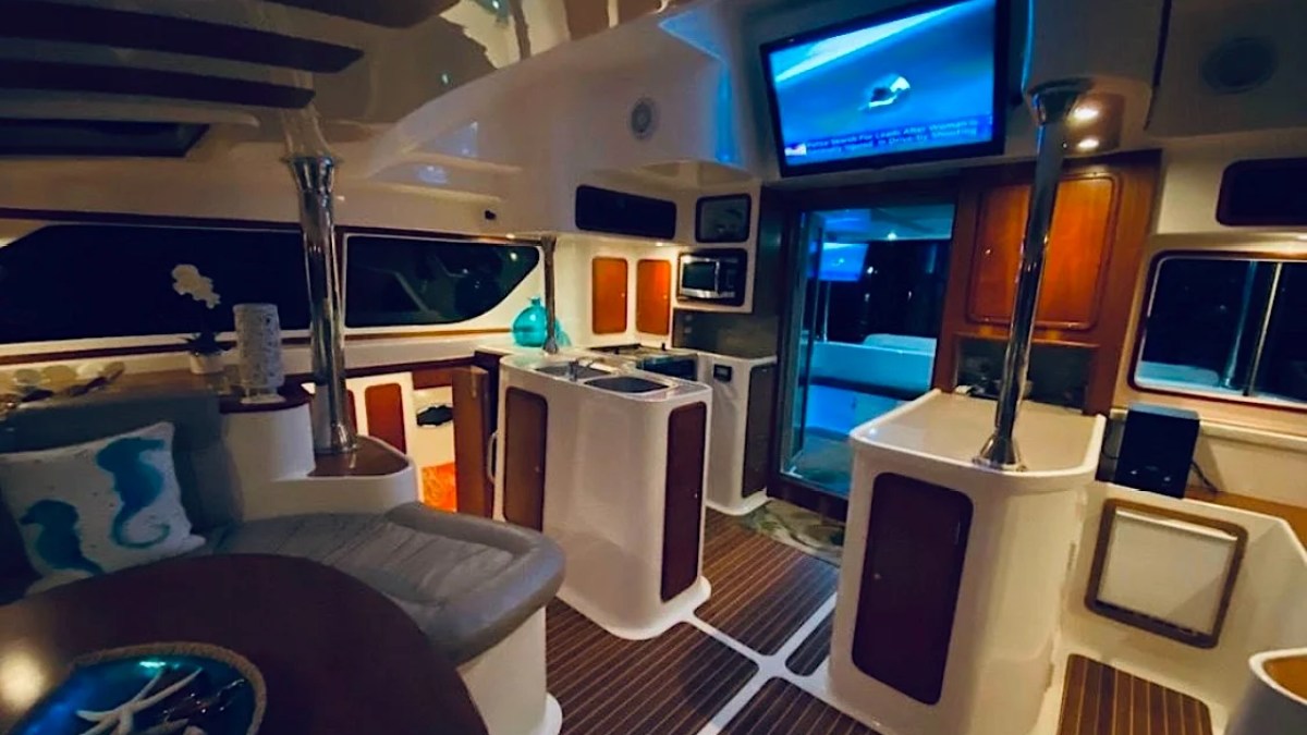 This 50 foot AfriCat Yacht Charter showcases an illuminated luxury salon with dining seating, galley counters, entertainment screen, and ambient evening lighting while cruising near Fort Myers and Sanibel Island.