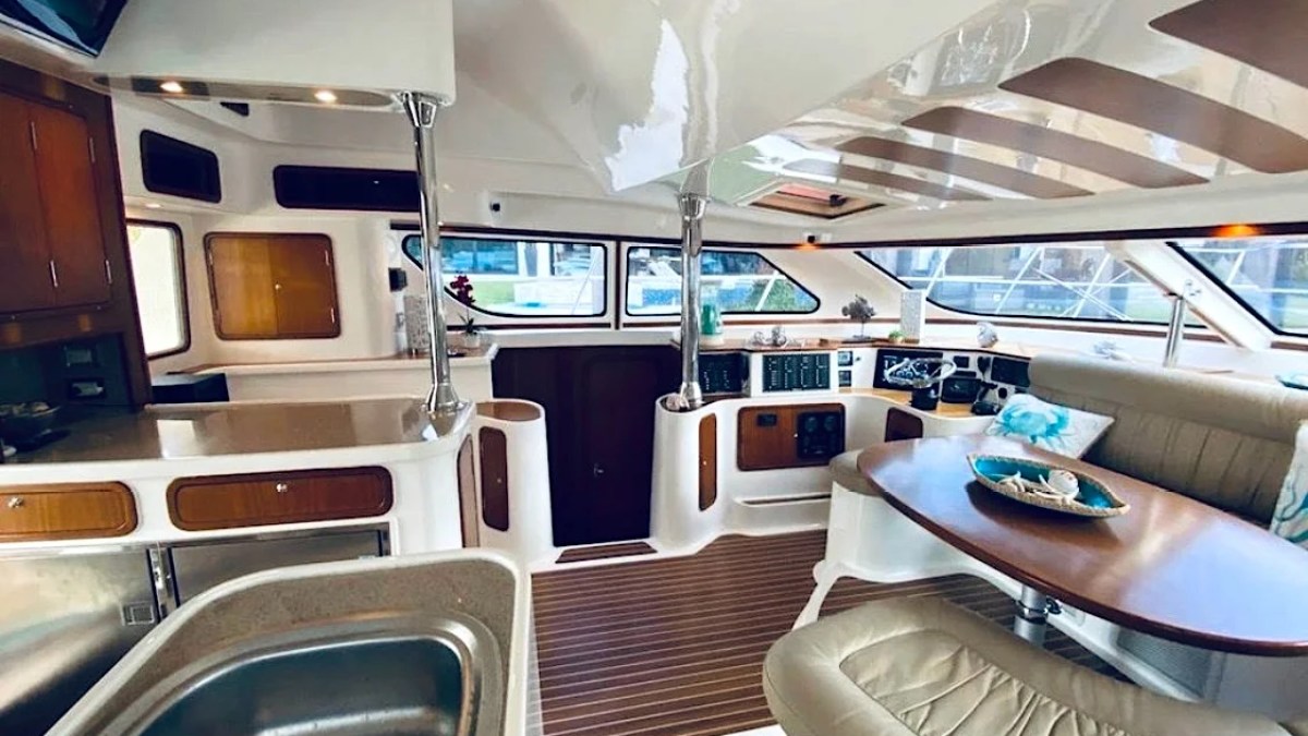 This 50 foot AfriCat Yacht Charter features an open-concept salon with dining seating, interior helm controls, galley countertops, and panoramic windows while docked in Fort Myers near Southwest Florida waterways.