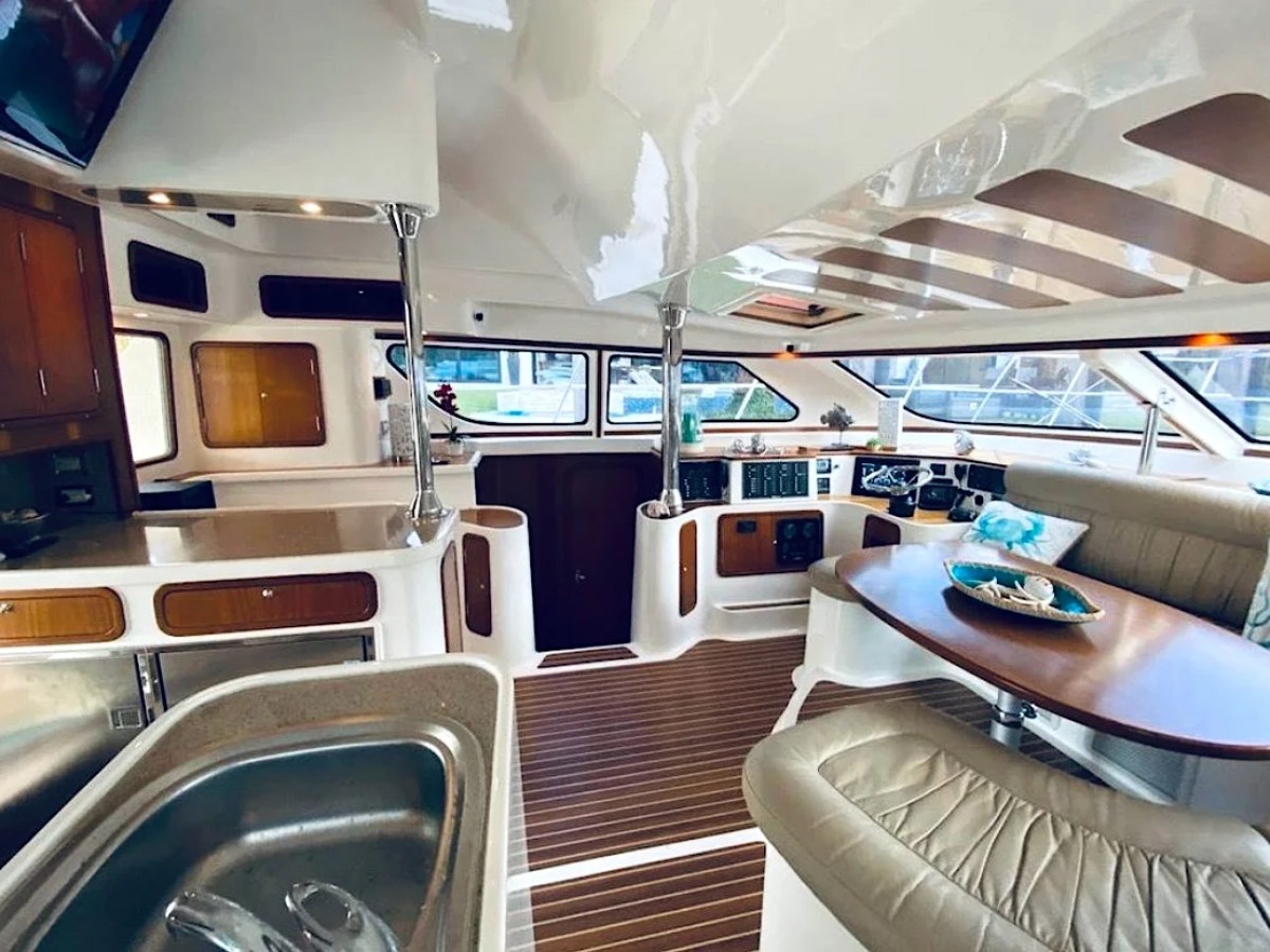 This 50 foot AfriCat Yacht Charter features an open-concept salon with dining seating, interior helm controls, galley countertops, and panoramic windows while docked in Fort Myers near Southwest Florida waterways.