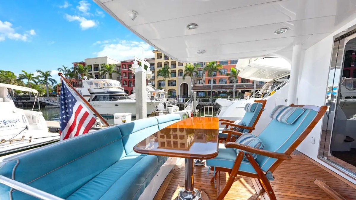 64' Hatteras Yacht Charter aft deck lounge featuring cushioned seating, teak decking, waterfront marina views, and shaded outdoor dining space in Marco Island.