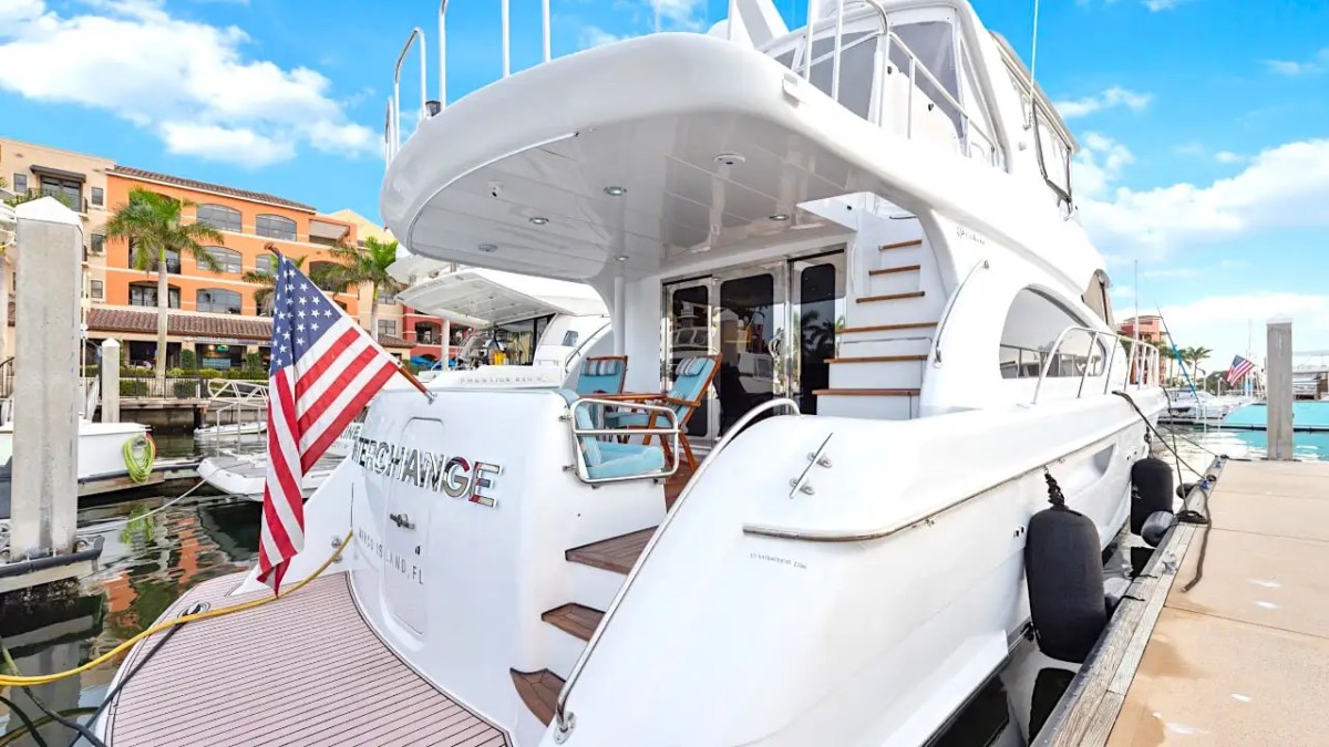 64' Hatteras Yacht Charter docked at a Marco Island marina featuring the aft deck entrance, teak swim platform, flybridge access stairs, and waterfront surroundings.
