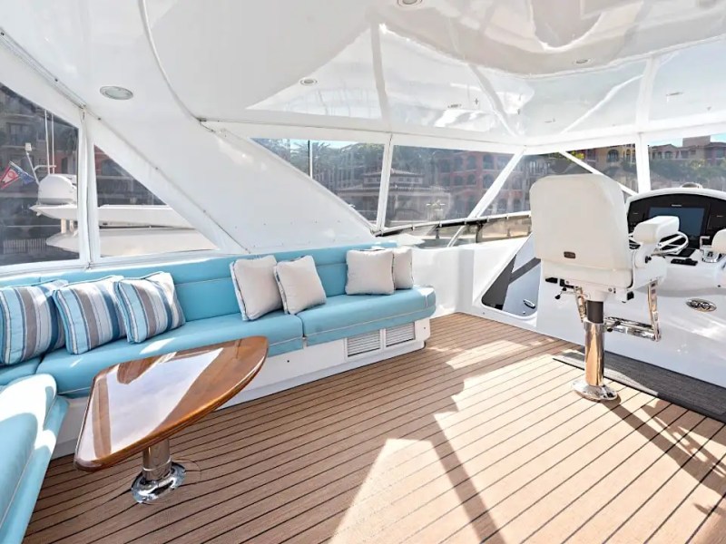 64' Hatteras Yacht Charter enclosed flybridge featuring wraparound lounge seating, teak-style decking, dual helm chairs, and panoramic marina views in Marco Island.