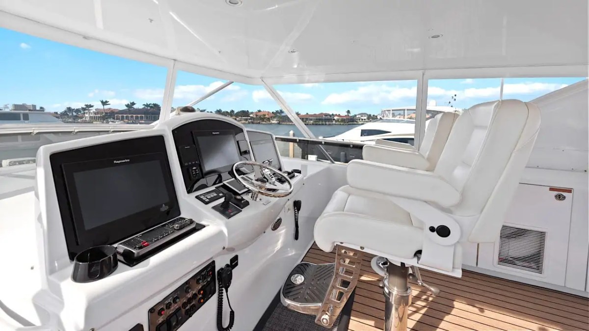 64' Hatteras Yacht Charter flybridge helm station featuring dual captain's chairs, navigation displays, teak-style decking, and panoramic waterfront views in Marco Island.