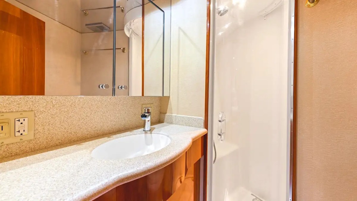 Guest bathroom aboard a 64' Hatteras Yacht Charter featuring a full-size shower, vanity sink, mirrored storage, premium fixtures, and elegant yacht finishes.
