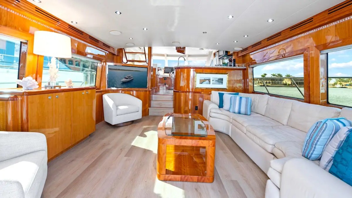 64' Hatteras Yacht Charter salon featuring expansive lounge seating, panoramic windows, glossy wood cabinetry, and an open-concept layout overlooking Marco Island waterways.