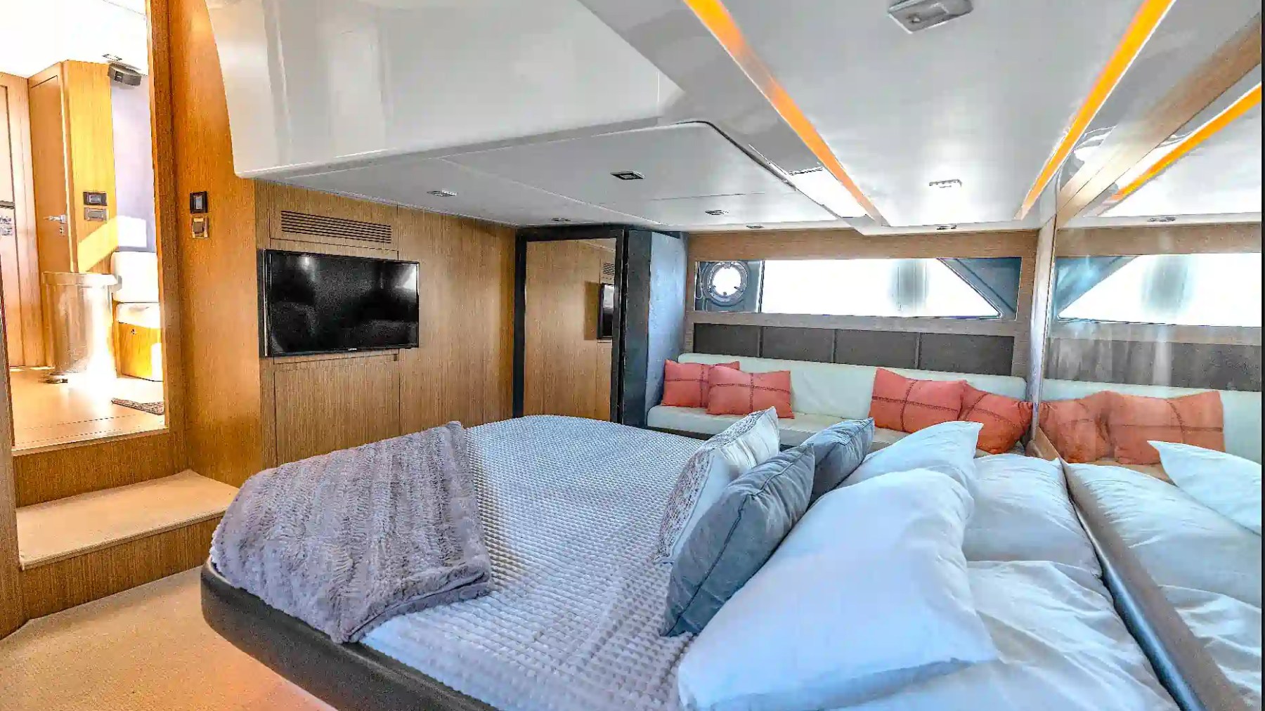 Spacious master stateroom aboard a 50' Azimut Yacht Charter featuring a large berth, mirrored wall panels, lounge seating, television, and contemporary wood finishes in Miami.