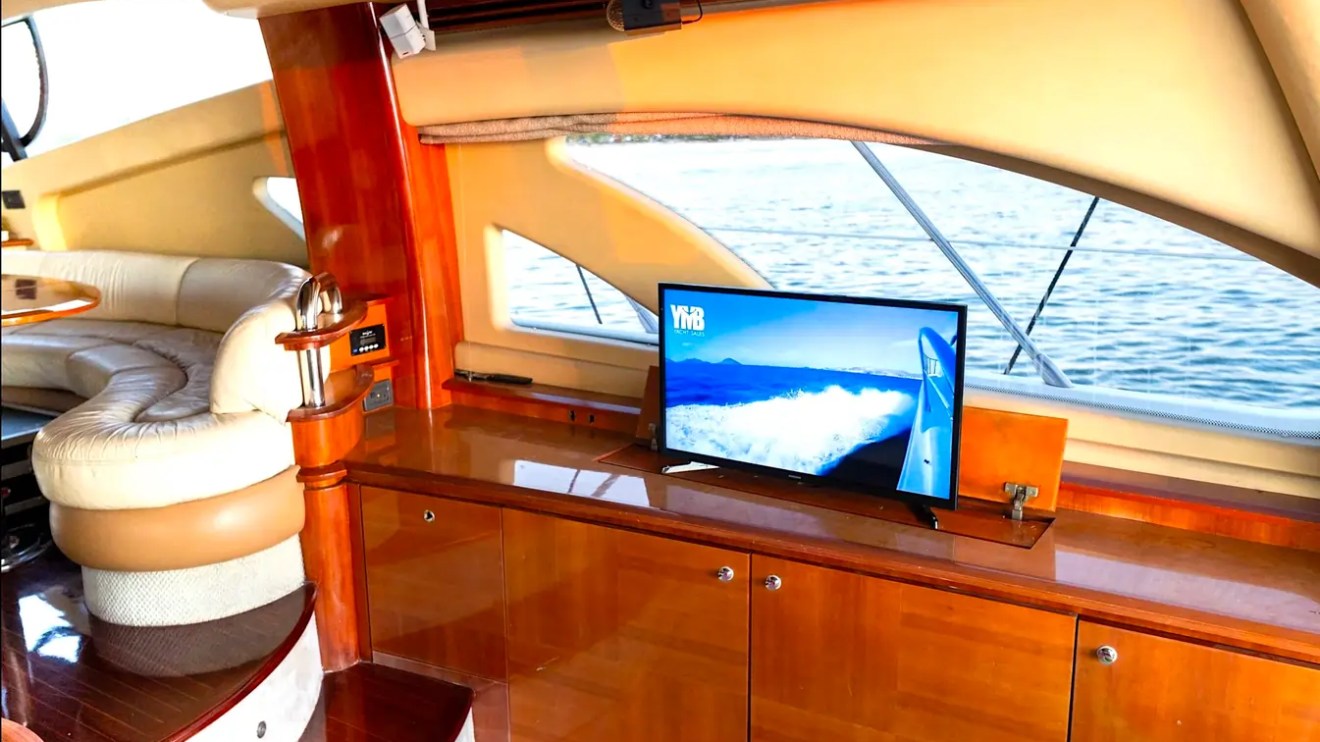 57' Azimut Yacht Charter salon entertainment center featuring a retractable TV, premium wood cabinetry, and elegant lounge seating in Miami.