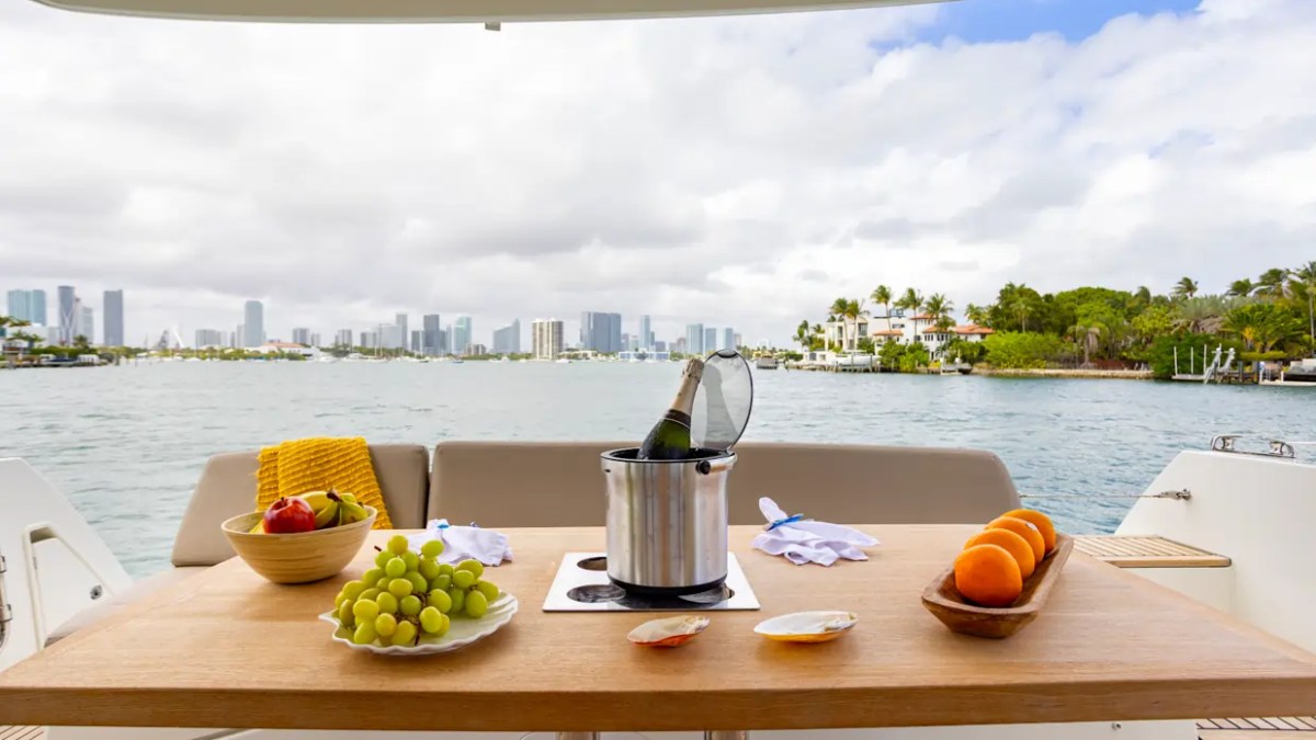 58' Prestige Yacht Charter aft deck dining with champagne, fresh fruit, and panoramic Biscayne Bay views overlooking the Miami skyline.