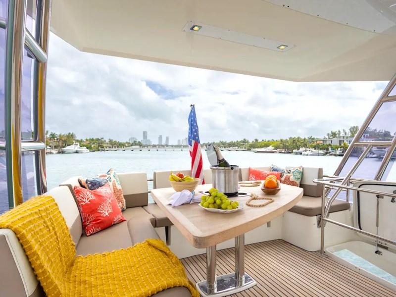 58' Prestige Yacht Charter aft deck lounge with waterfront dining, champagne, and skyline views along Miami Beach and Biscayne Bay.