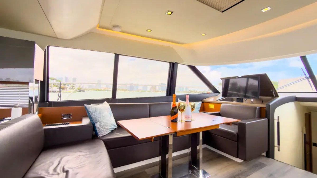 58' Prestige Yacht Charter enclosed flybridge skylounge with premium lounge seating, dining table, and panoramic Biscayne Bay views near the Miami skyline.