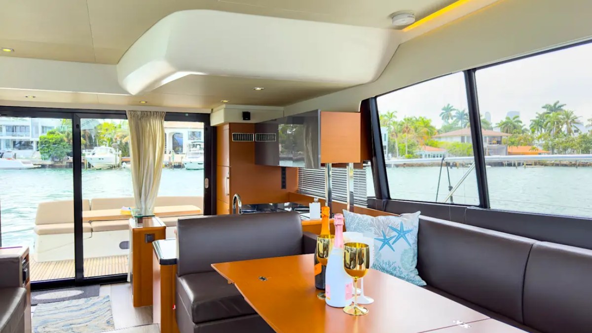 58' Prestige Yacht Charter luxury skylounge dining area with panoramic windows, elegant seating, and modern galley overlooking Biscayne Bay near Miami Beach.