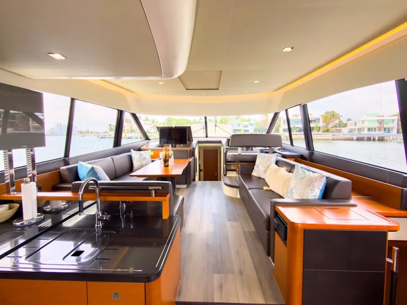 58' Prestige Yacht Charter enclosed skylounge featuring panoramic windows, luxury lounge seating, modern galley, and elegant entertaining space cruising Biscayne Bay in Miami.