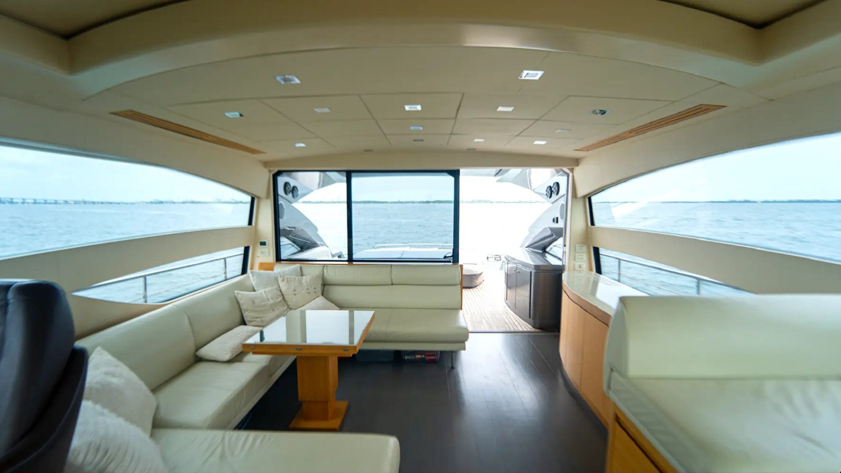 64' Pershing Yacht Charter showcasing the bright contemporary main salon with panoramic windows, plush wraparound seating, and seamless cockpit access while cruising Miami's Biscayne Bay.