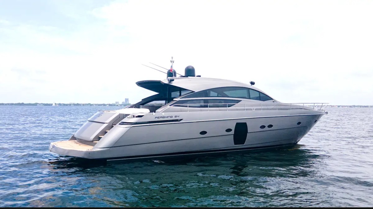 64' Pershing Yacht Charter viewed from the port aft quarter cruising Biscayne Bay near Miami, showcasing its sleek Italian profile, spacious swim platform, and luxurious open cockpit.