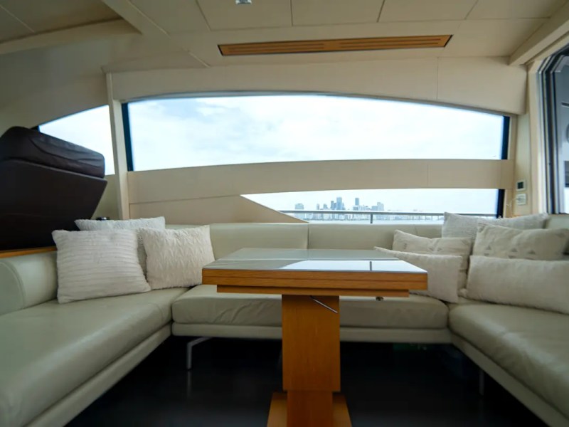 64' Pershing Yacht Charter elegant salon lounge with wraparound leather seating, panoramic windows, and dining table overlooking the Miami skyline on Biscayne Bay.