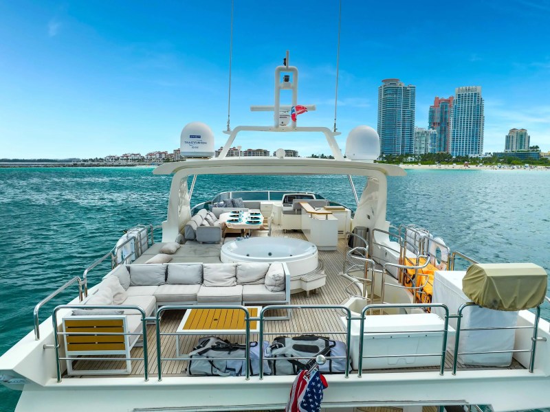 84' Azimut Yacht Charter aft deck lounge anchored near Miami Beach, featuring an elevated spa tub, wraparound seating, outdoor dining area, and skyline waterfront views.