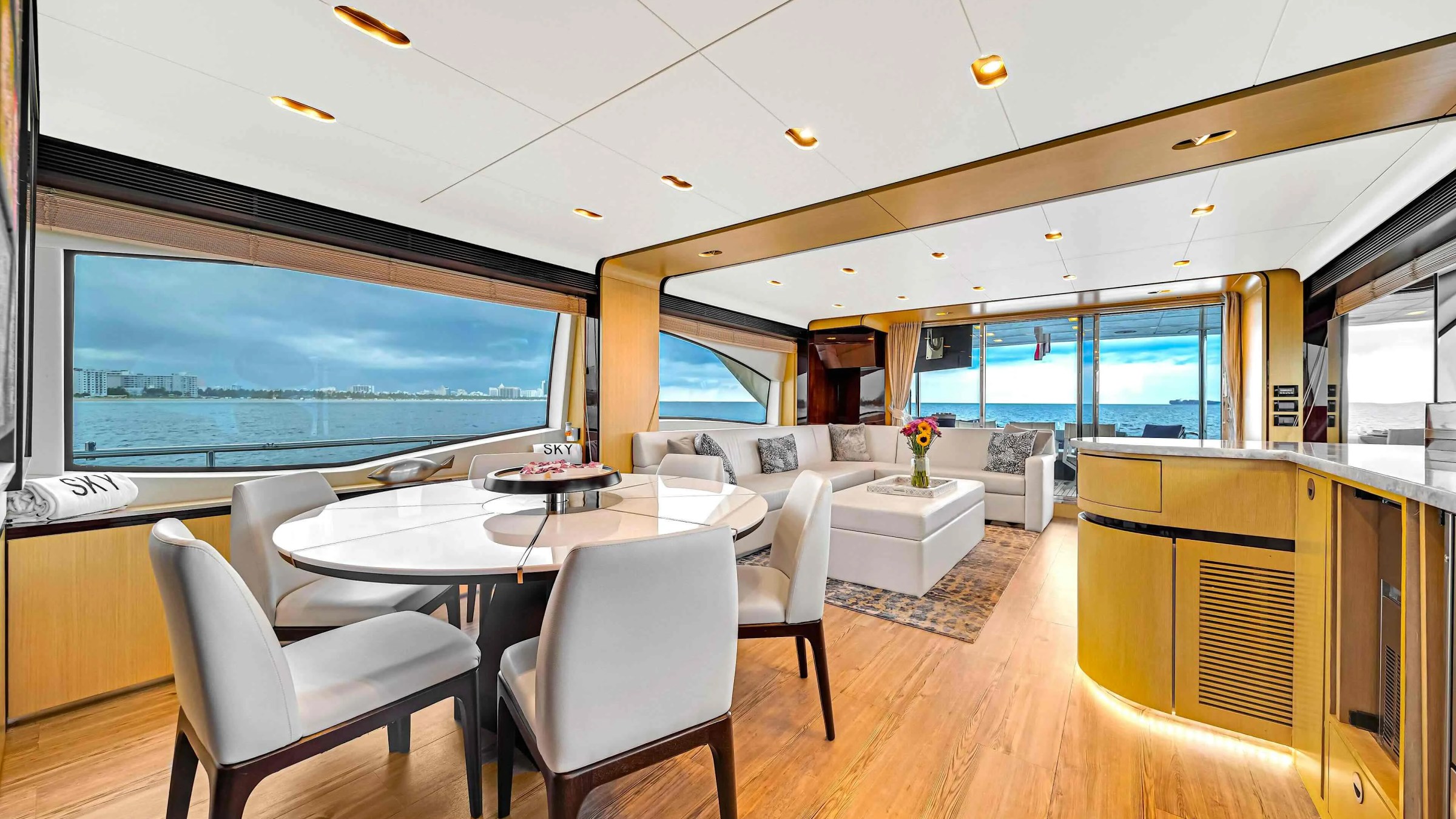 84' Azimut Yacht Charter interior dining salon featuring a round formal dining table, panoramic waterfront windows, contemporary furnishings, and Miami coastal views.