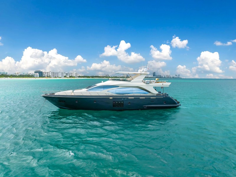 84' Azimut Yacht Charter anchored in crystal-clear waters off Miami Beach, showcasing a sleek side profile, flybridge deck, and panoramic South Florida coastal scenery.