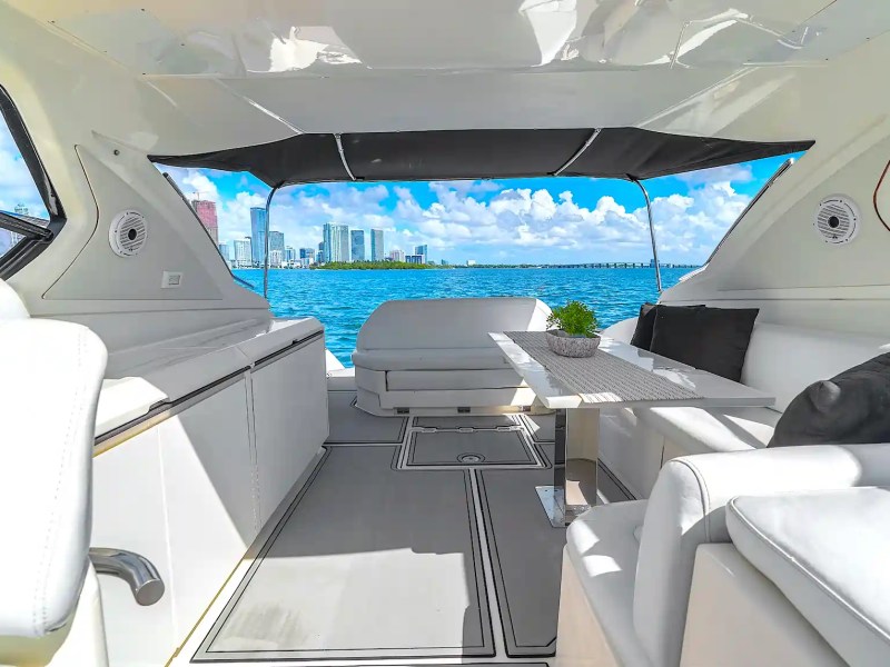 Aft cockpit lounge aboard a 50' Azimut Yacht Charter featuring white seating, dining table, shaded canopy, and panoramic Biscayne Bay skyline views in Miami.