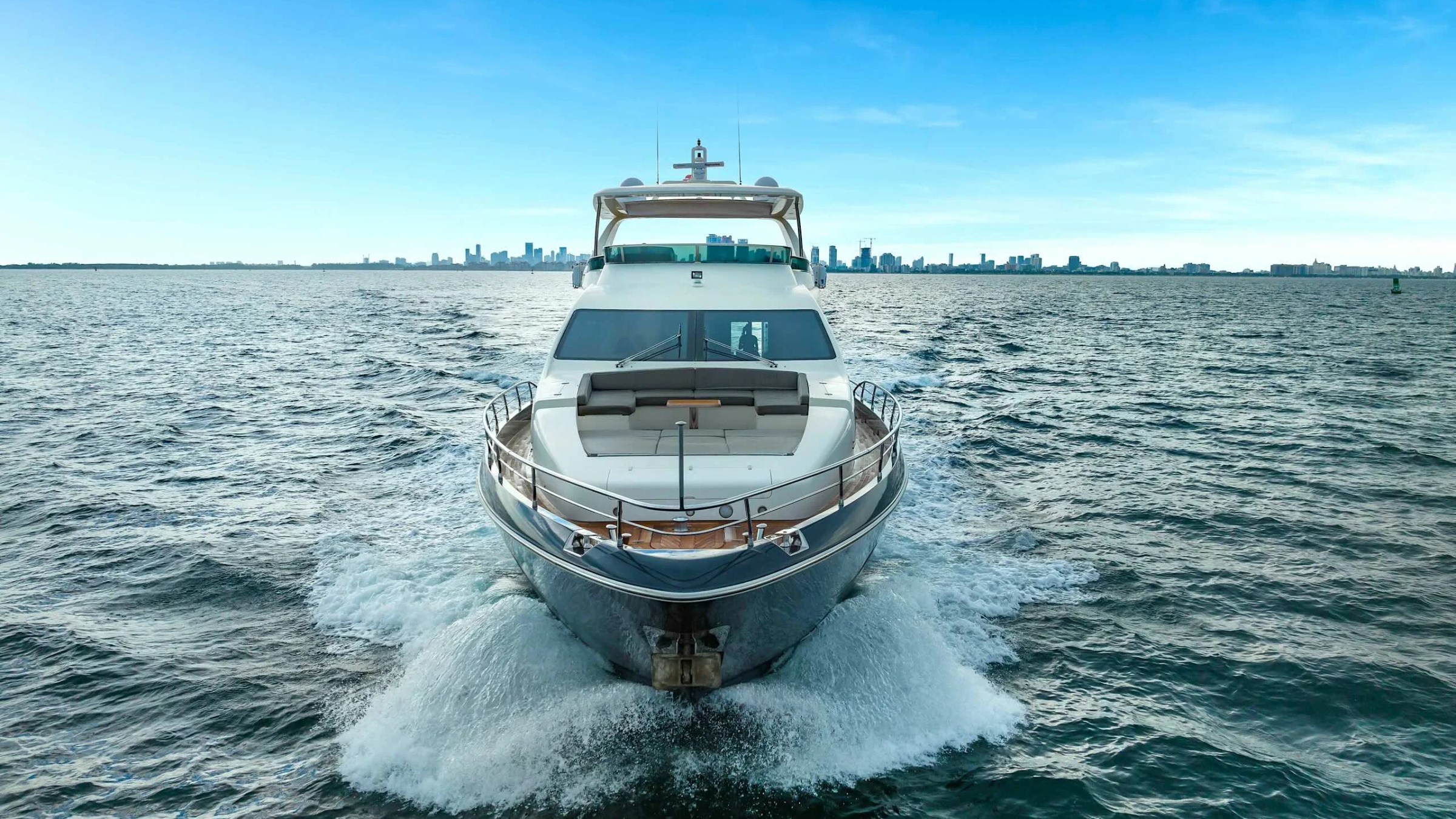 84' Azimut Yacht Charter cruising through Biscayne Bay with a head-on perspective showcasing the spacious bow lounge, sleek profile, and Miami skyline in the distance.