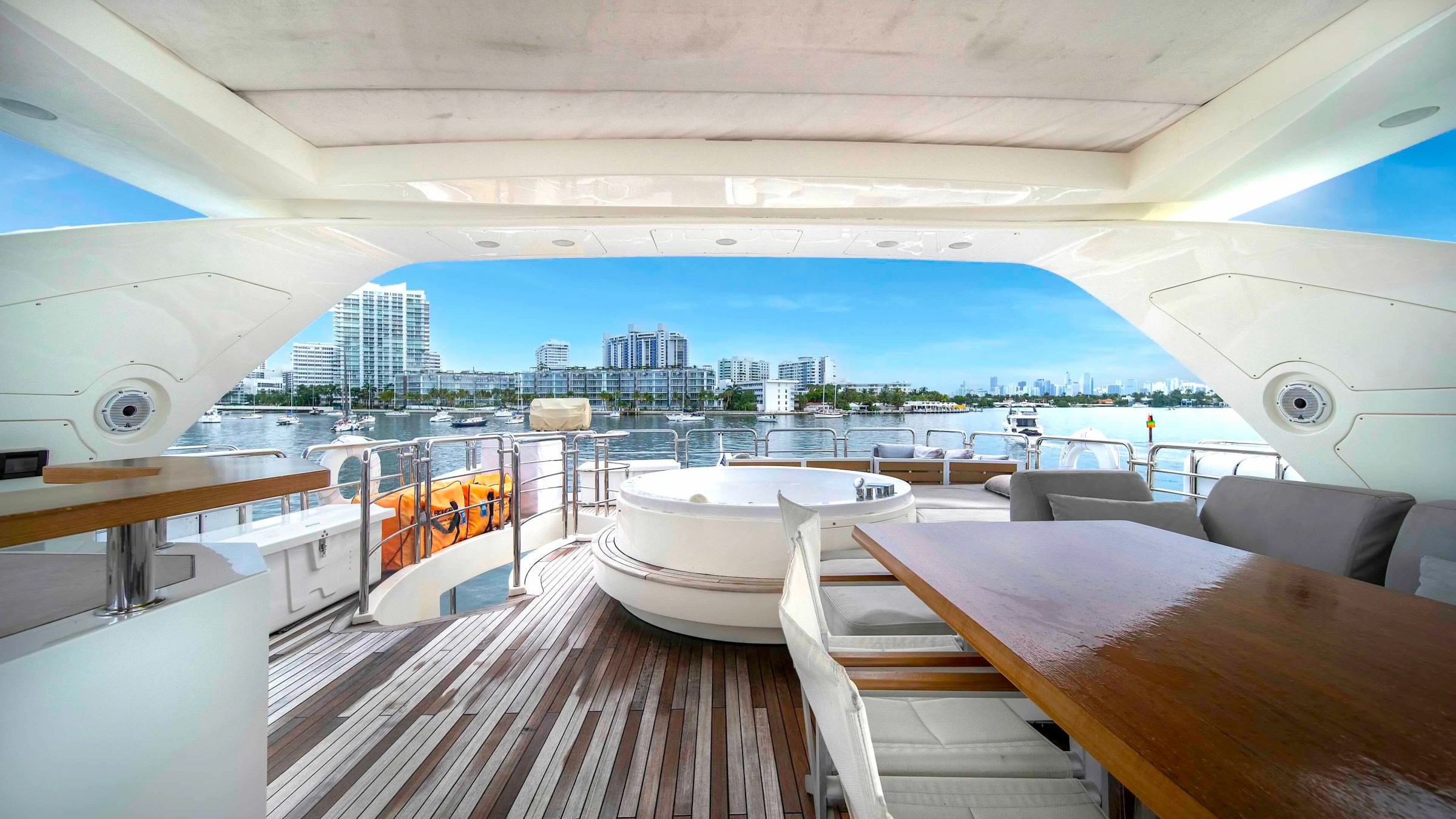 84' Azimut Yacht Charter flybridge entertaining area overlooking Biscayne Bay, featuring a dining table, spa tub, lounge seating, teak decking, and Miami waterfront views.