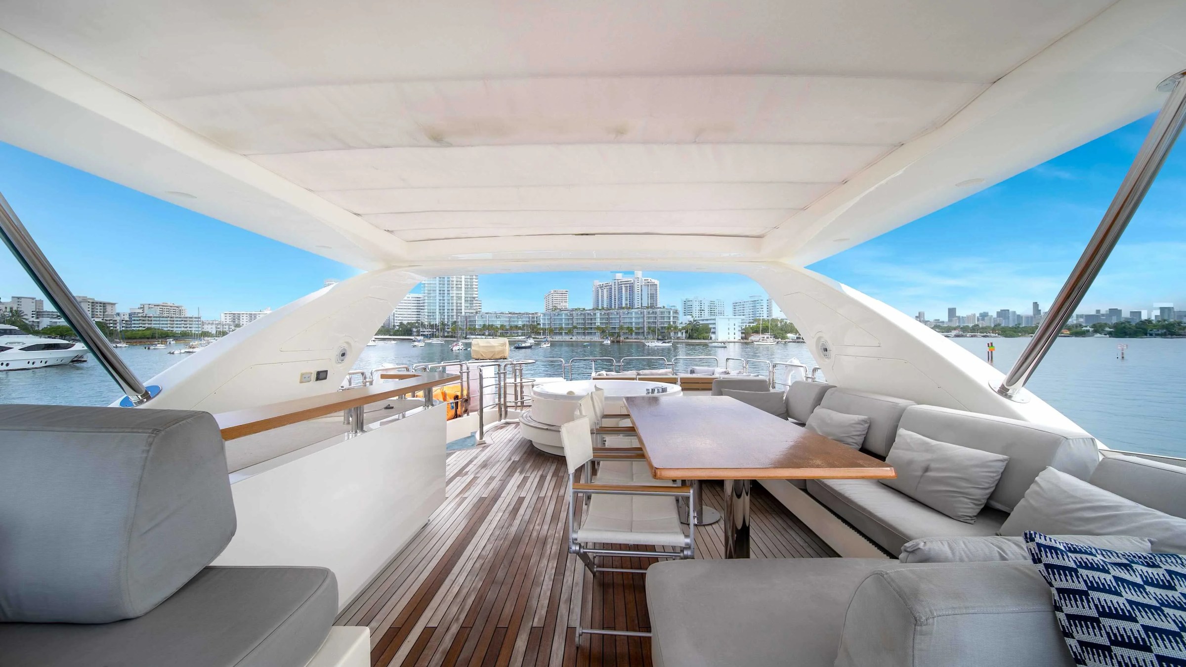 84' Azimut Yacht Charter flybridge lounge overlooking Miami waterways, featuring wraparound seating, alfresco dining table, teak decking, and skyline views across Biscayne Bay.