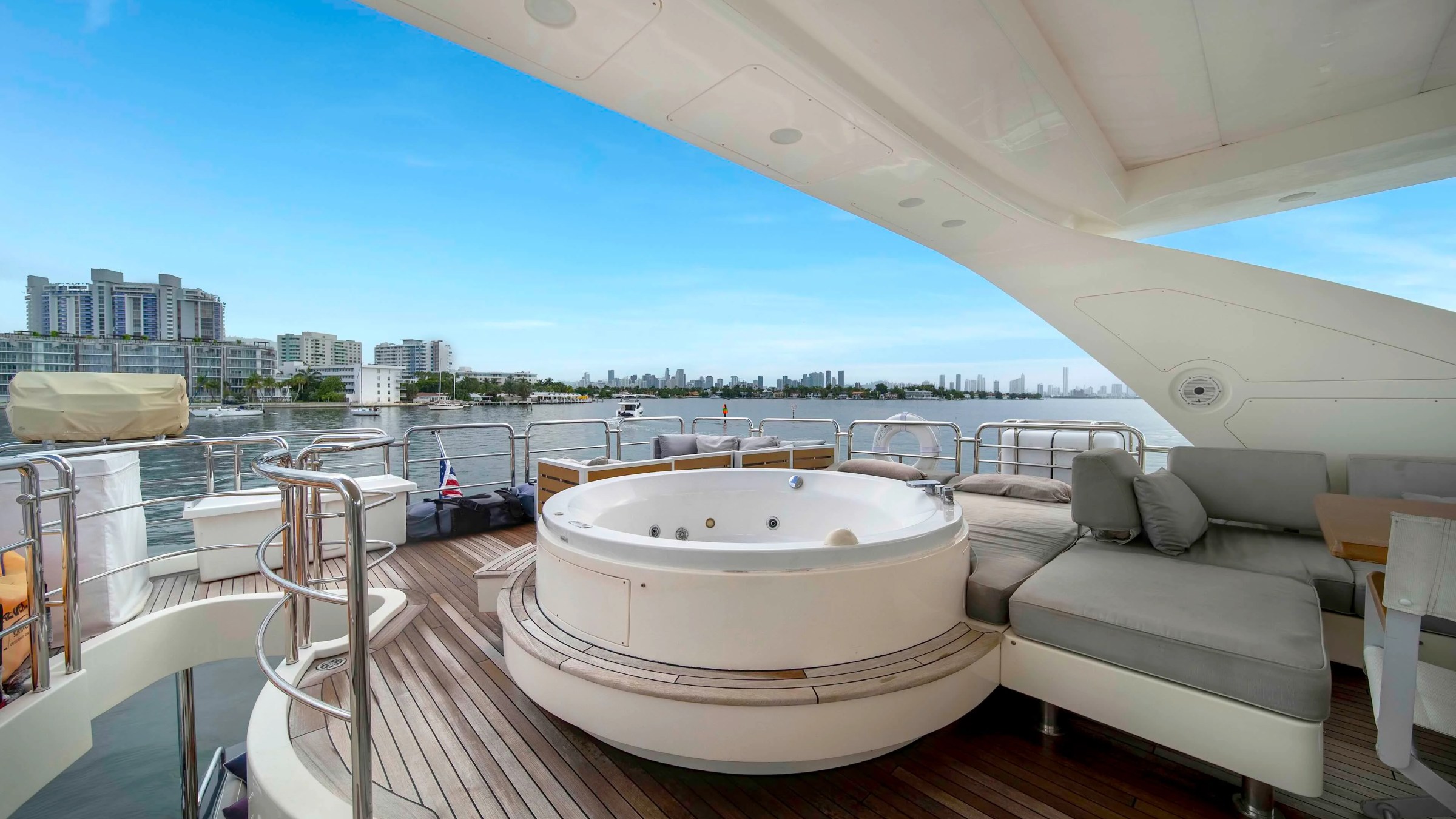 84' Azimut Yacht Charter flybridge entertainment deck overlooking Biscayne Bay, featuring a built-in spa tub, sun lounge seating, teak decking, and Miami skyline views.