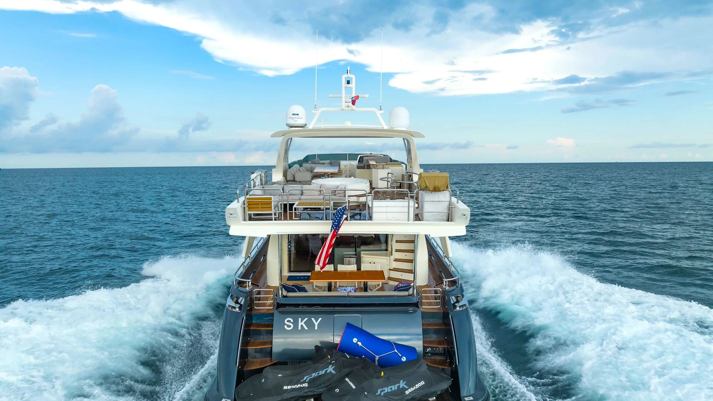 84' Azimut Yacht Charter viewed from astern while cruising through South Florida waters, showcasing the spacious flybridge, swim platform, and dramatic wake behind the yacht.