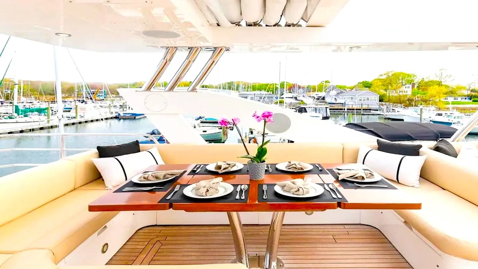 75' Sunseeker Yacht Charter aft deck dining area featuring wraparound seating, teak flooring, table settings, and marina views near Nassau in The Bahamas.