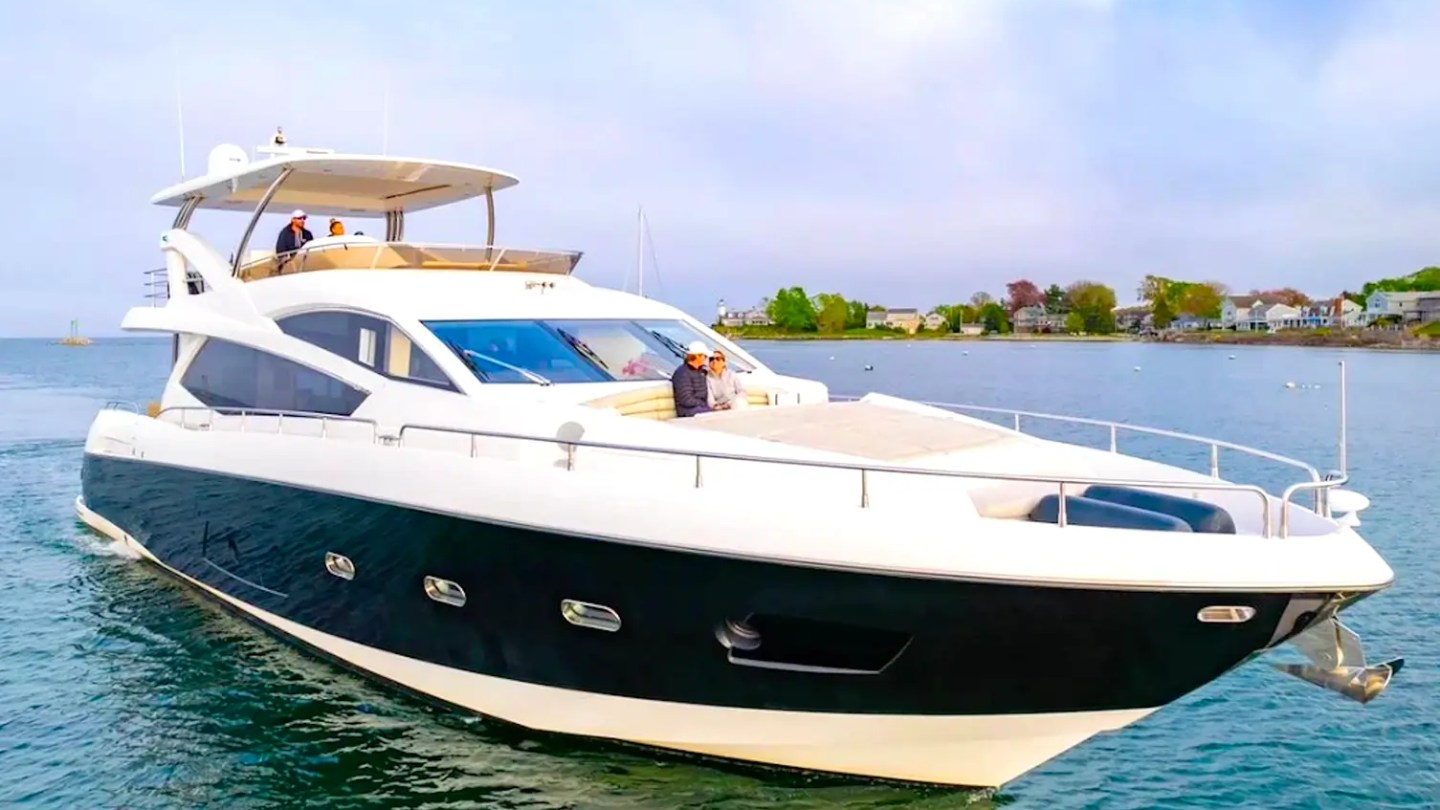 75' Sunseeker Yacht Charter cruising near Nassau with guests relaxing on the foredeck lounge, showcasing a sleek black hull, flybridge, and calm waterfront scenery.
