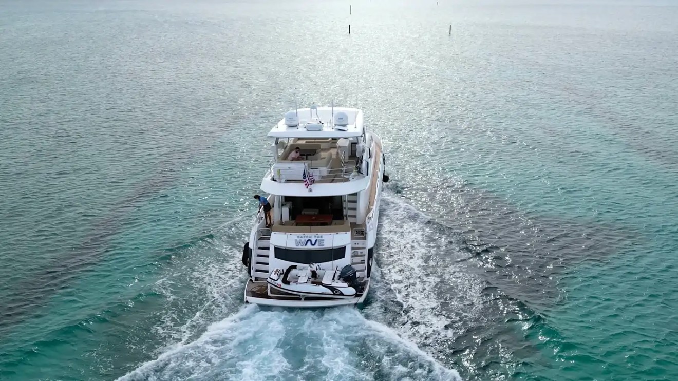 75' Sunseeker Yacht Charter captured from an offshore aerial perspective cruising through the turquoise waters near Nassau, showcasing the flybridge, wake trail, and onboard tender.