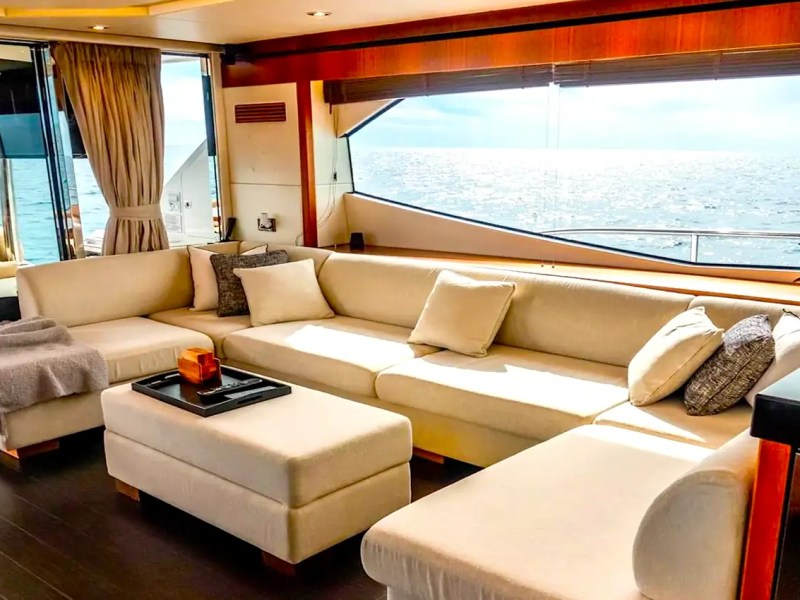 75' Sunseeker Yacht Charter salon featuring wraparound cream seating, panoramic ocean-view windows, wood finishes, and natural light while cruising near Nassau.