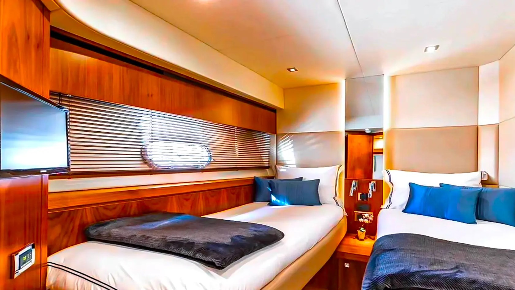 75' Sunseeker Yacht Charter guest cabin featuring twin berths, wood cabinetry, hull-side windows, and modern entertainment amenities while docked in Nassau.