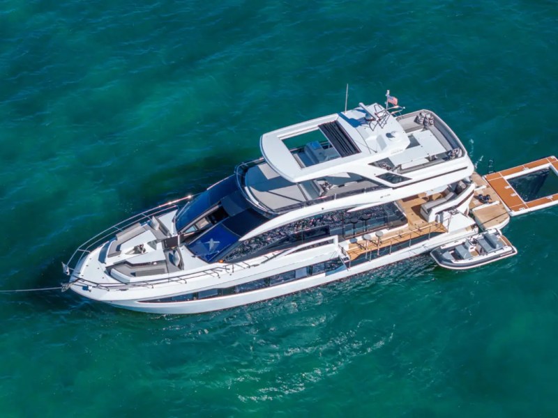 68' Galeon Yacht Charter captured from a coastal aerial showing the foldout beach club terraces expansive flybridge and floating swim platform anchored off Key Biscayne on Biscayne Bay.