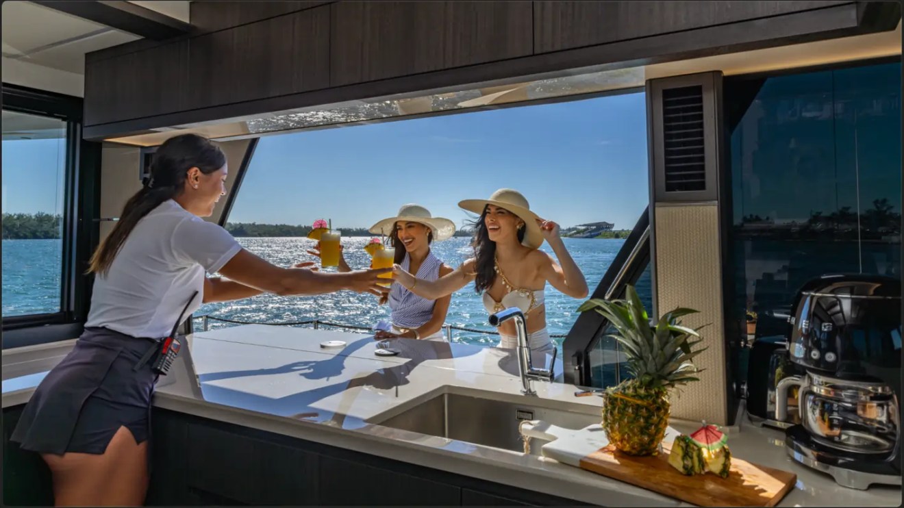 68' Galeon Yacht Charter featuring the galley pass-through serving guests with refreshments beside panoramic windows while cruising near Key Biscayne on Biscayne Bay.