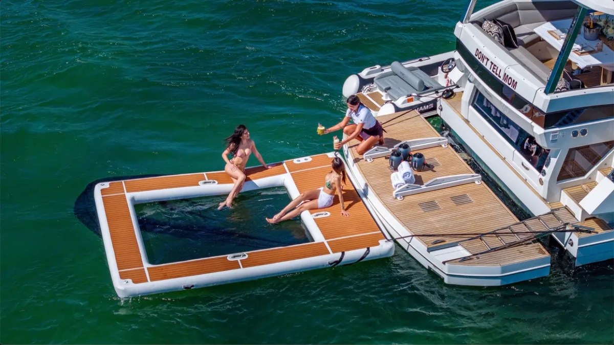 68' Galeon Yacht Charter featuring the hydraulic swim platform and inflatable ocean pool with guests relaxing beside the yacht while anchored off Key Biscayne on Biscayne Bay.