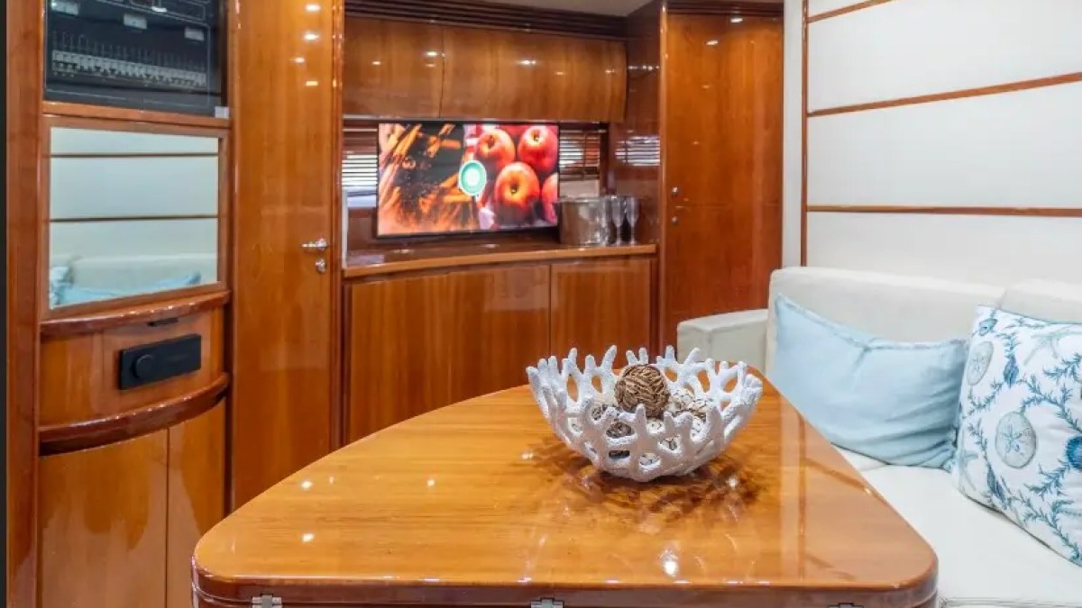 50' Pershing Yacht Charter salon showcasing a polished wood dining table, wraparound lounge seating, entertainment center, and premium interior finishes in Miami.