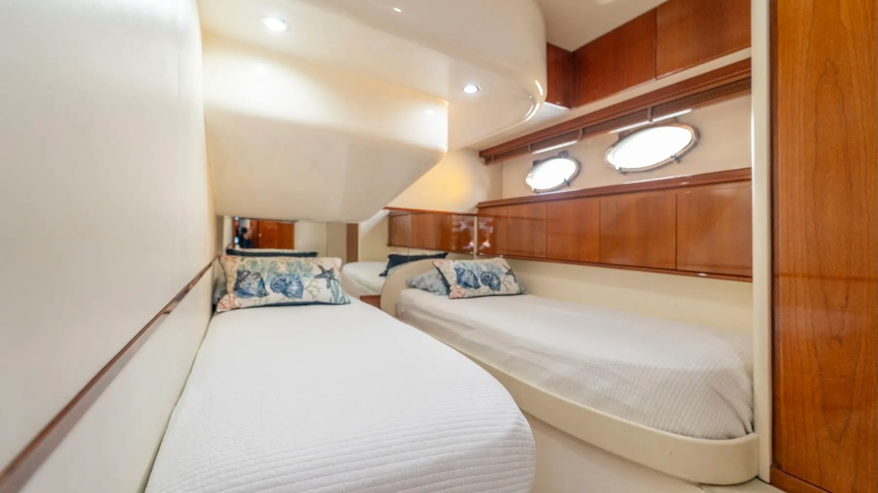 50' Pershing Yacht Charter guest cabin with twin beds warm wood cabinetry oval portlights and contemporary accommodations while cruising in Miami on Biscayne Bay.