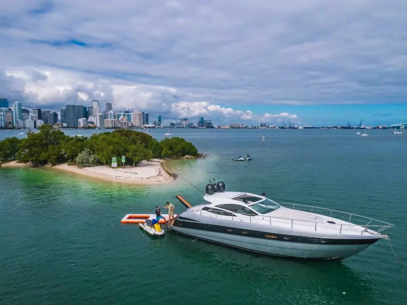 50' Pershing Yacht Charter anchored near a tropical island with a Magic Carpet floating platform and Downtown Miami skyline views.