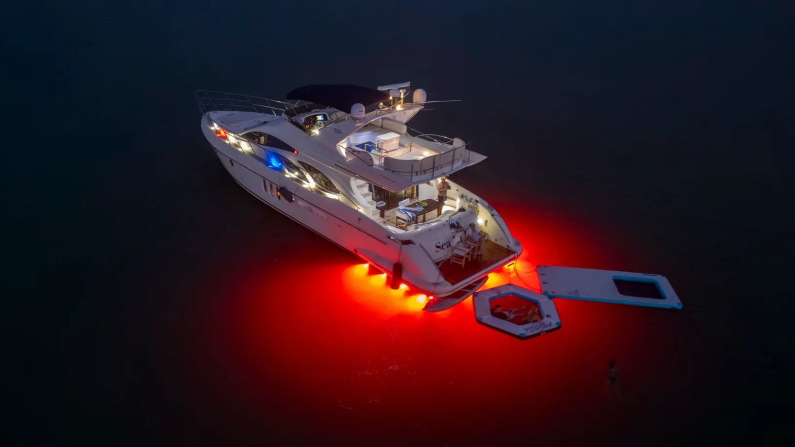 65' Azimut Yacht Charter at night with red underwater lights, Magic Carpet & floating lounge on Biscayne Bay in Miami.